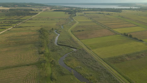 Vista-Aérea-Del-Hermoso-Río-Sinuoso-Y-Las-Pintorescas-Tierras-De-Cultivo-Abiertas-Y-El-Lago-Con-Carretera