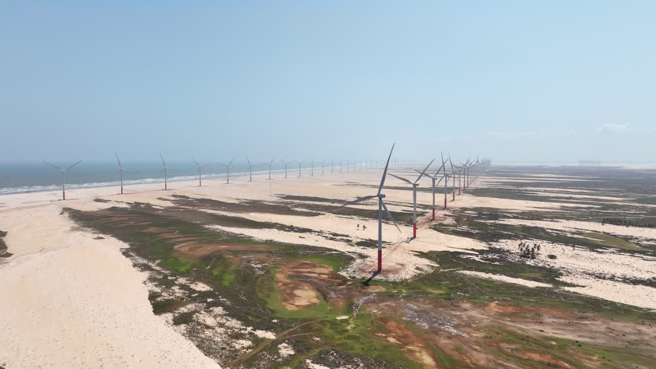 Wind turbines on sandy terrain along the coast in Delta do Parnaíba, Brazil. Backward drone aerial