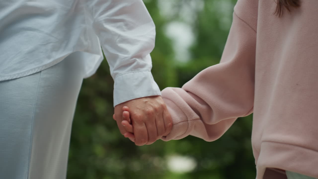 屋外で手を取り合って歩く母と娘。母親は日陰の庭の小道を安全に子供を導く。穏やかな母と娘が、緑豊かな美しい小道を安心して散歩を楽しむ。