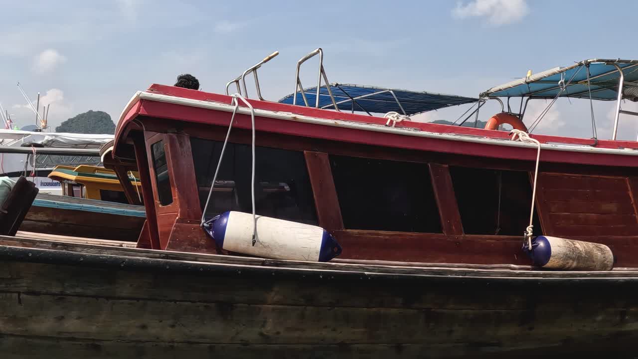 A person walks along the deck of a moored wooden boat under a clear sky.