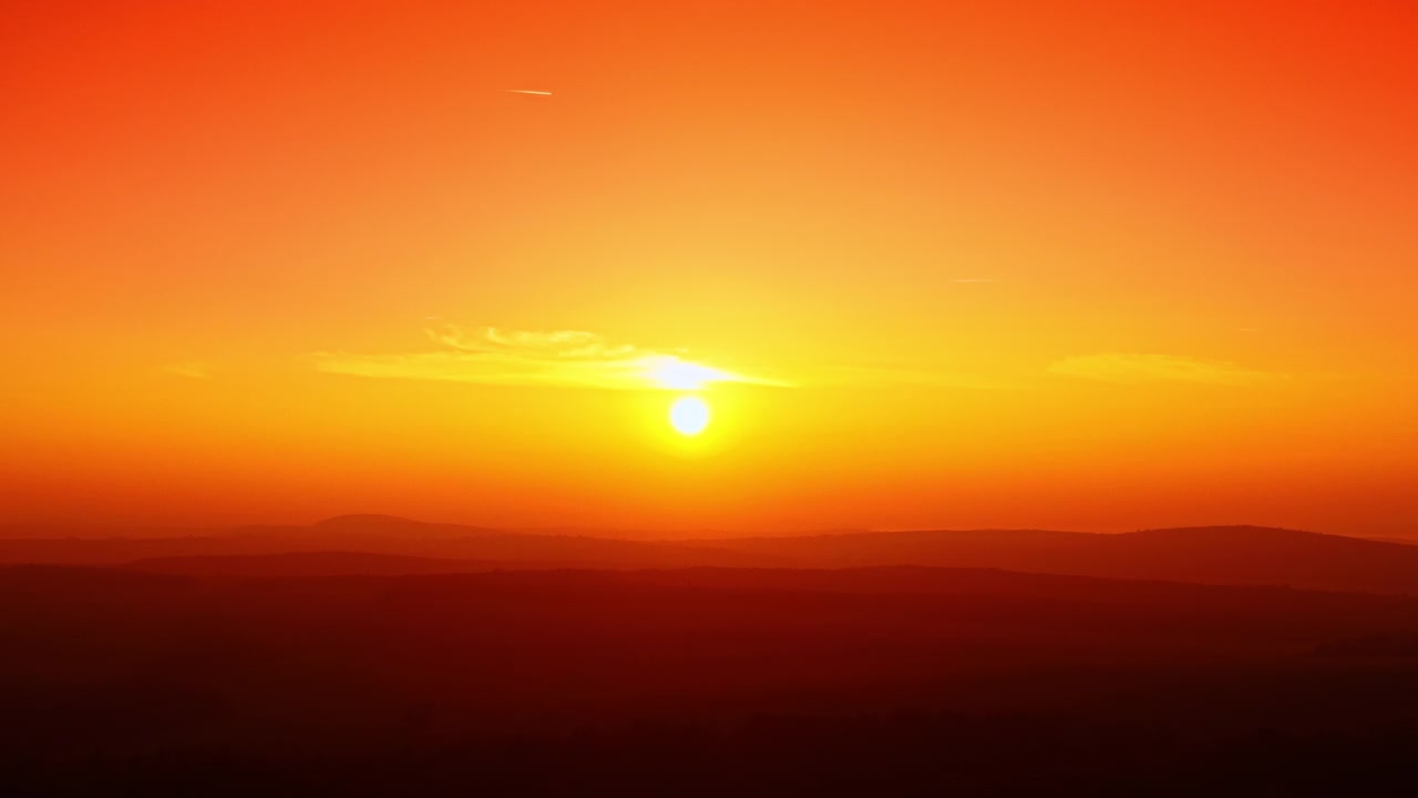 Golden sunset over layered mountain hills. Warm orange and yellow gradient sky with sun disc touching the horizon silhouette.