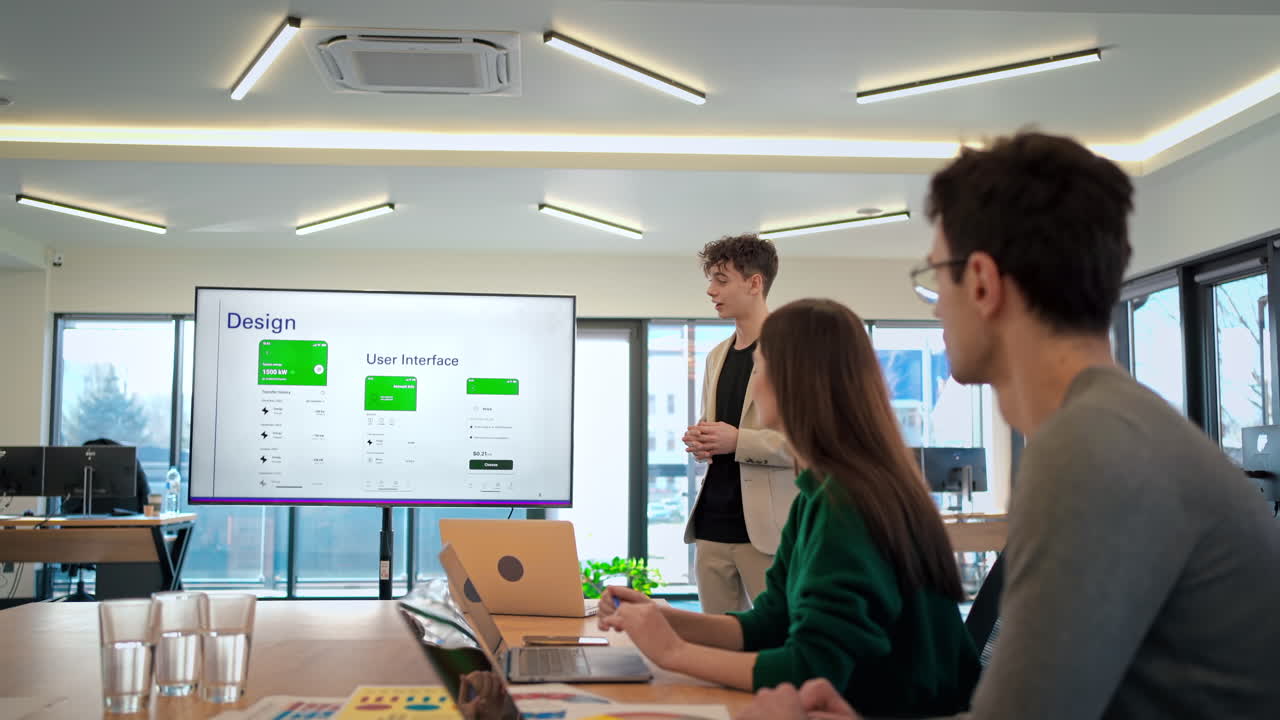 Young worker leading business meeting in an office, discussing business affairs with other workers using a big display with info