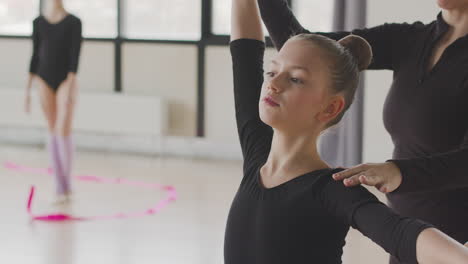 female teacher corrects the arm and head position of the gymnastic girl in ballet class