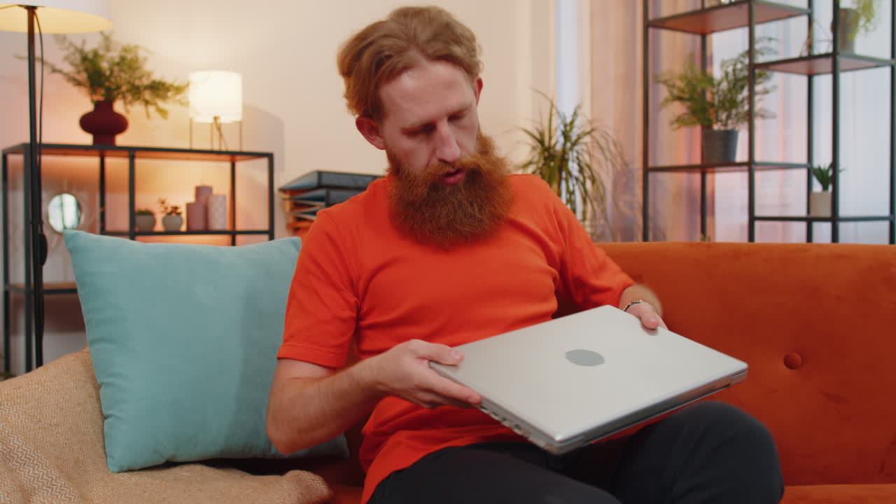 молодой человек-фрилансер лежит на диване, закрывая ноутбук после окончания работы в гостиной дома