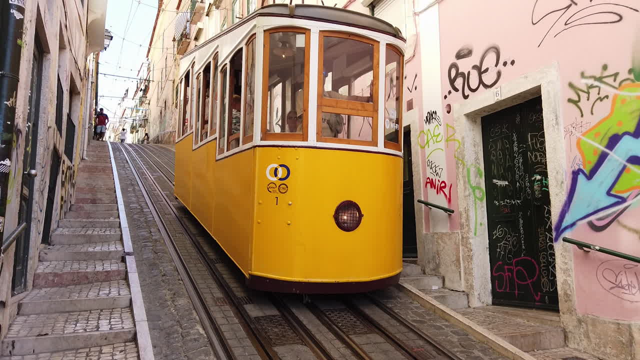 Iconic yellow Tram 28 traveling through historic streets in Alfama, Lisbon descending along graffiti covered walls