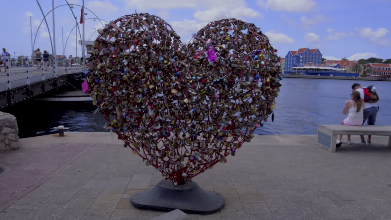 In love couple watch the sea with big shaped hearth beside with padlocks. Curaçao, Willemstad. Passion