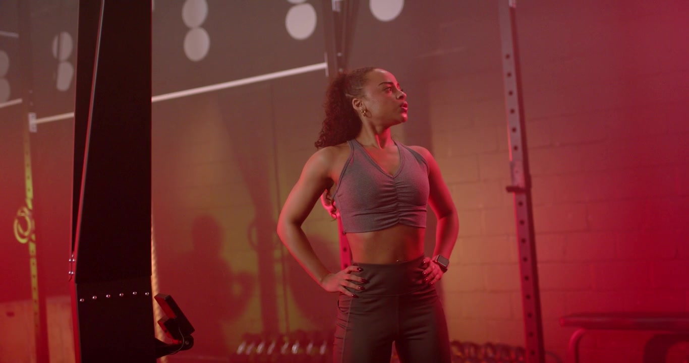 Adult African American woman breathing after set, checking smartwatch, adjusting stance at gym rig