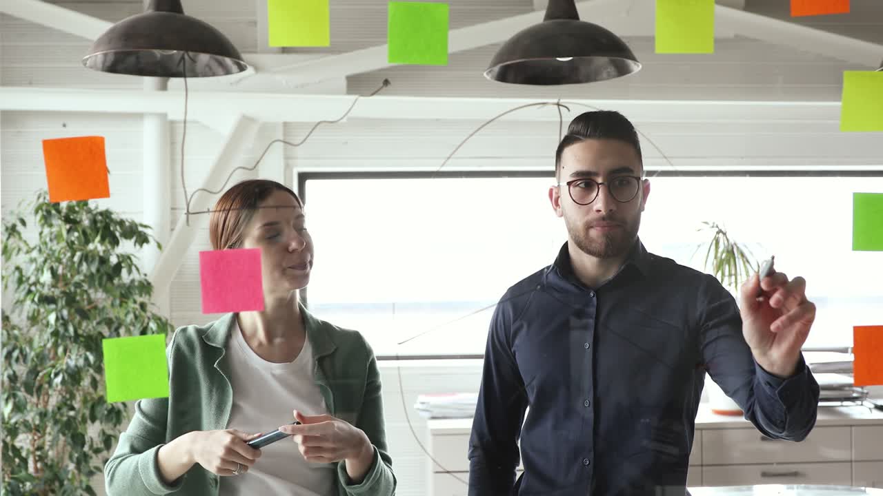 Skilled young arabian male manager drawing charts on glass wall.