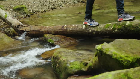 traverser le ruisseau de montagne sur un arbre tombé une personne franchit un obstacle seuls les pieds dans les chaussures sont vi