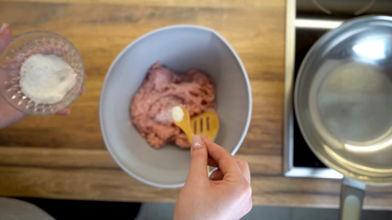 mujer agregando una cucharada de sal a un tazón de carne picada