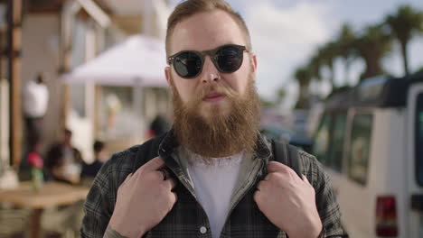 retrato de un hombre hipster barbudo con gafas de sol sonriendo con confianza en la playa