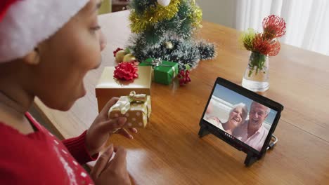 Afroamerikanische-Frau-Mit-Weihnachtsmütze-Nutzt-Tablet-Für-Weihnachtsvideoanruf-Mit-Paar-Auf-Dem-Bildschirm