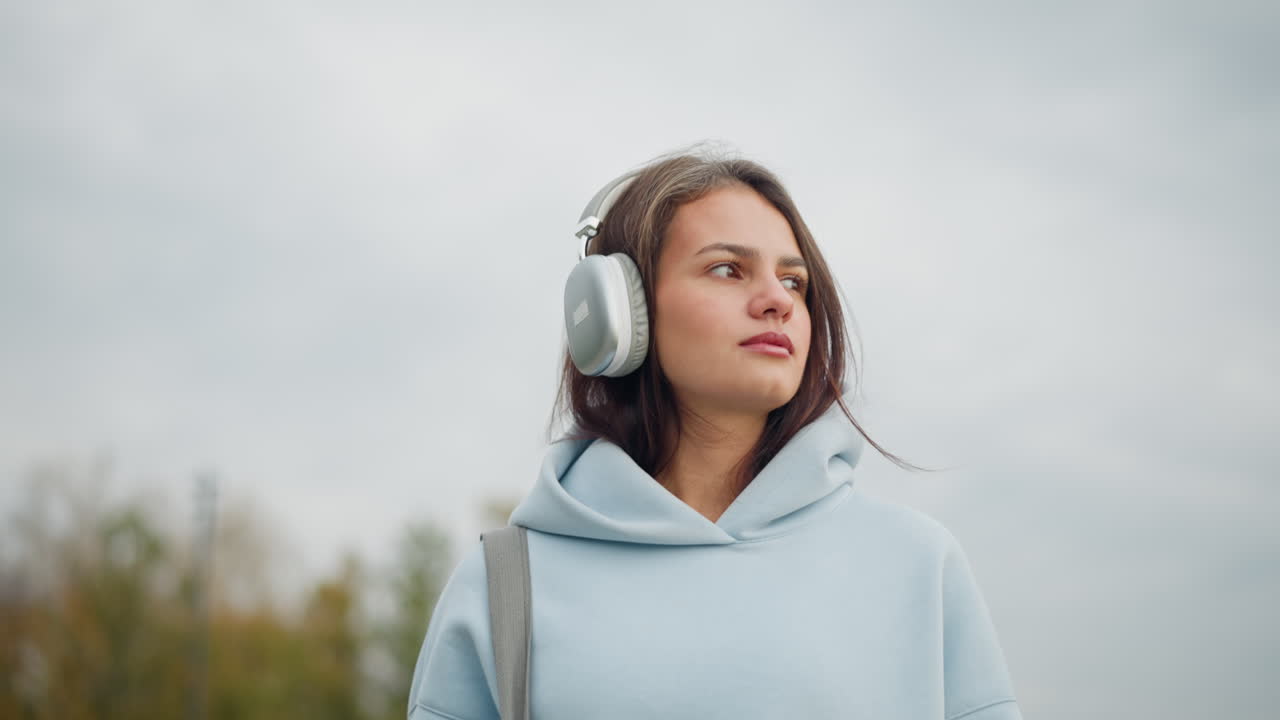 Pretty woman in casual wear and headphones carrying bag as she walks in calm outdoor environment, peaceful stroll with focus on her enjoying the surroundings in a relaxed manner