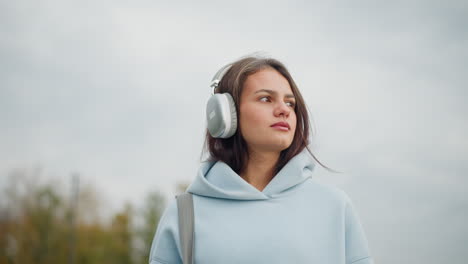 pretty woman in casual wear and headphones carrying bag as she walks in calm outdoor environment, peaceful stroll with focus on her enjoying the surroundings in a relaxed manner