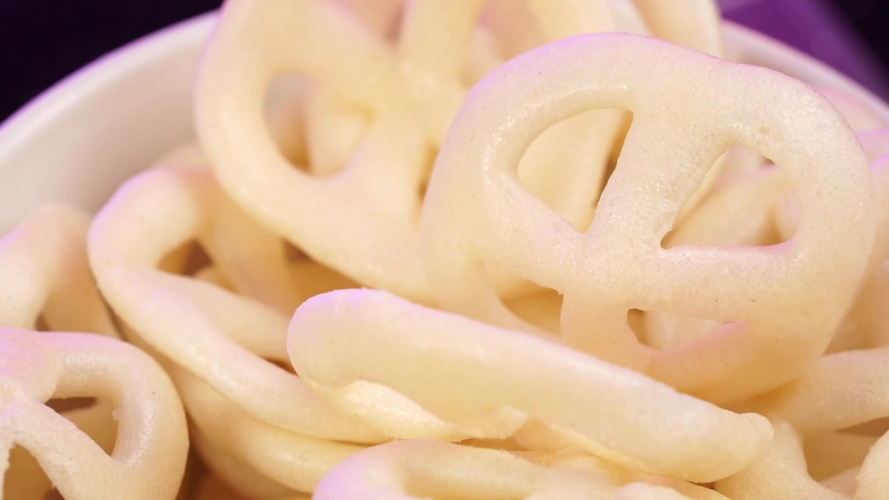 Primo piano dettagliato di croccanti snack fritti a forma di ruota in una ciotola, che mostrano la loro consistenza dorata e l'aspetto croccante, ideali per uno spuntino