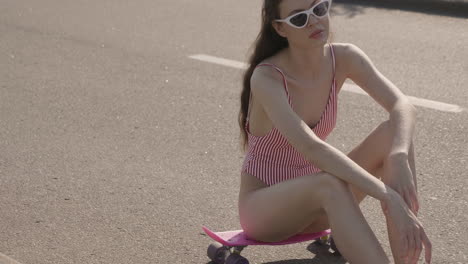 woman in swimsuit sitting on a skateboard on the street