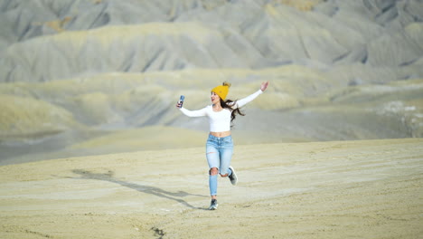 Joven-Mujer-Feliz-Corriendo-Con-Smartphone-Y-Grabando-Video-Selfie-En-El-Paisaje-Desértico-De-Utah