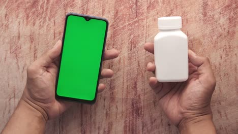 la mano sostiene un teléfono inteligente con pantalla verde y contenedor de pastillas médicas