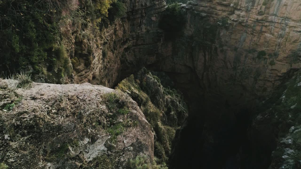 sensacional vista aérea de la formación rocosa del arco en el paisaje montañoso del líbano, un joven excursionista vestido con ropa deportiva se inclina sobre el acantilado, drones volando hacia atrás, día