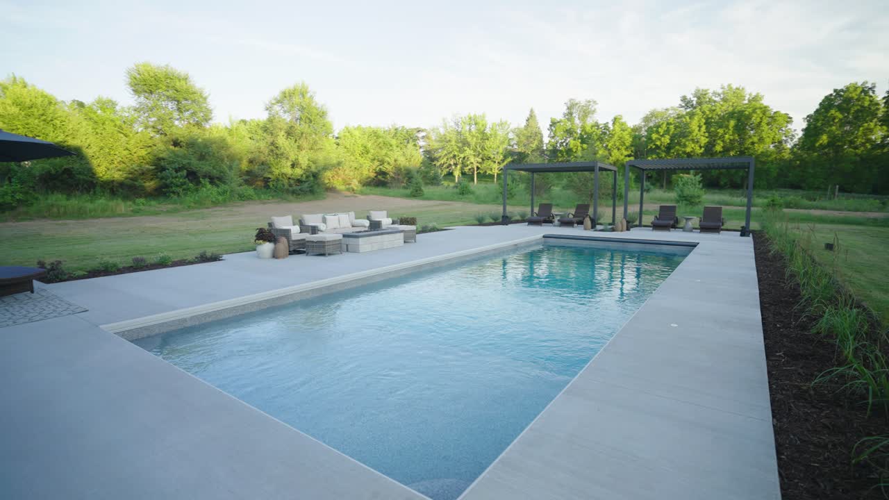 Moderne boligterrasse med pergolaer, loungemøbler og en glasfiberpool.