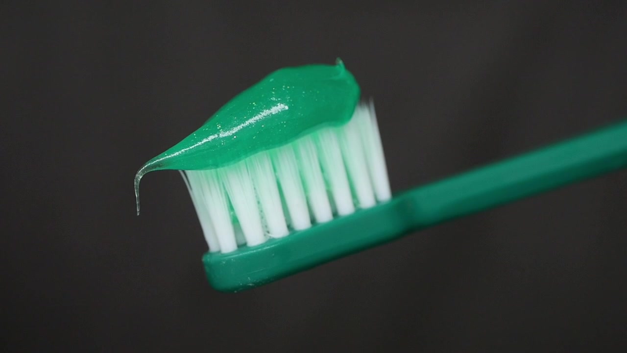 Pasta de dientes verde siendo exprimida sobre un cepillo de dientes verde