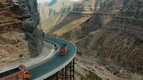 aerial over lorries driving along cpec road at fort munro in pakistan with reveal of sulaiman mountain valley views