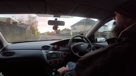 hombre barbudo conduciendo a través de las calles de las ciudades suburbanas británicas y la vista del tráfico desde la perspectiva del vehículo interior