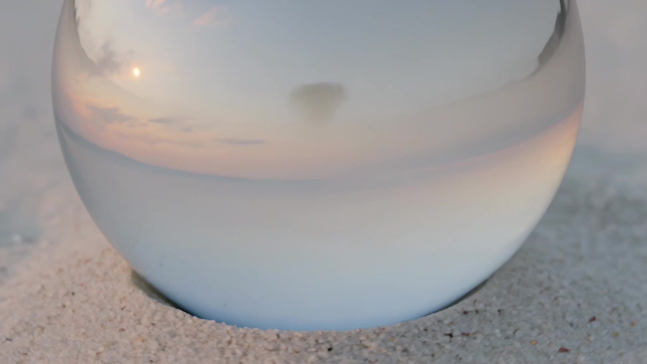 Shifting sunset light causing crystal sphere reflecting horizon, sun patch and dark spot on sand