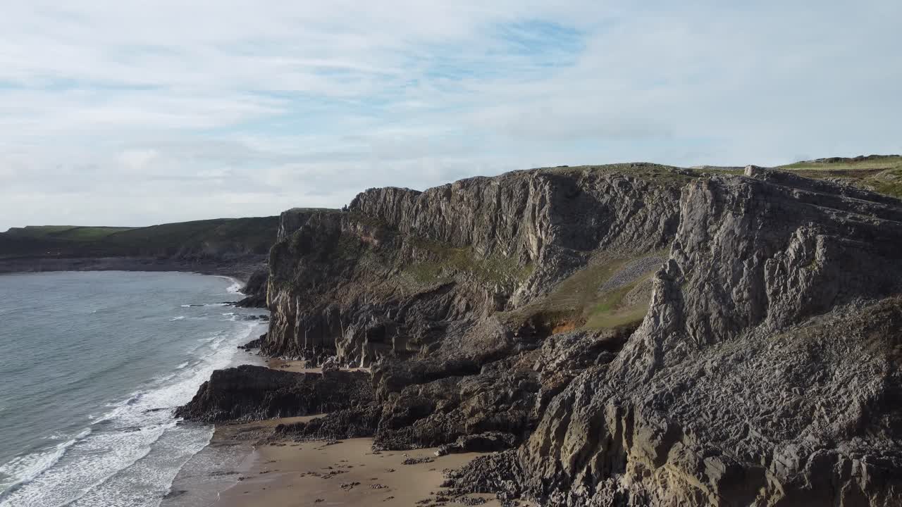 Aerial View of Coastal Cliffs as Drone Camera Slowly Descends to Reveal Golden Sandy Beach and Gentle Rolling Waves on Mewslade Bay Wales UK 4K