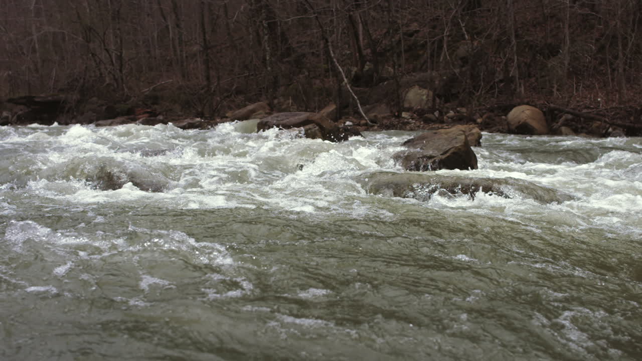 Super slow motion footage panning across the white water rapids of a creek after a heavy rain.