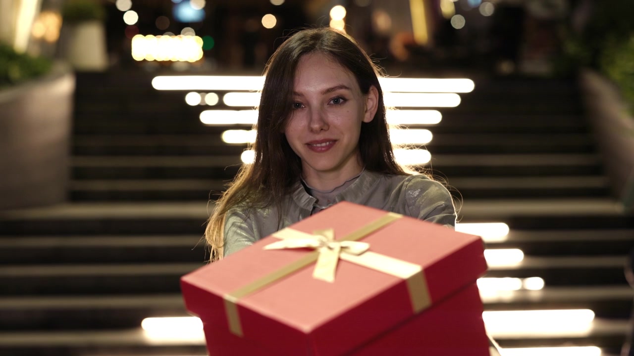 Giovane donna sorridente che porge una scatola regalo rossa di notte.