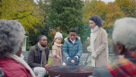 multi-generation family toasting marshmallows standing around firepit or barbeque in garden at home - shot in slow motion