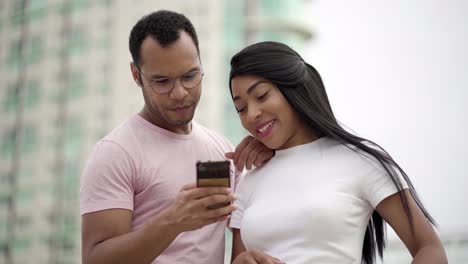 Smiling-multiracial-couple-talking-and-looking-at-smartphone