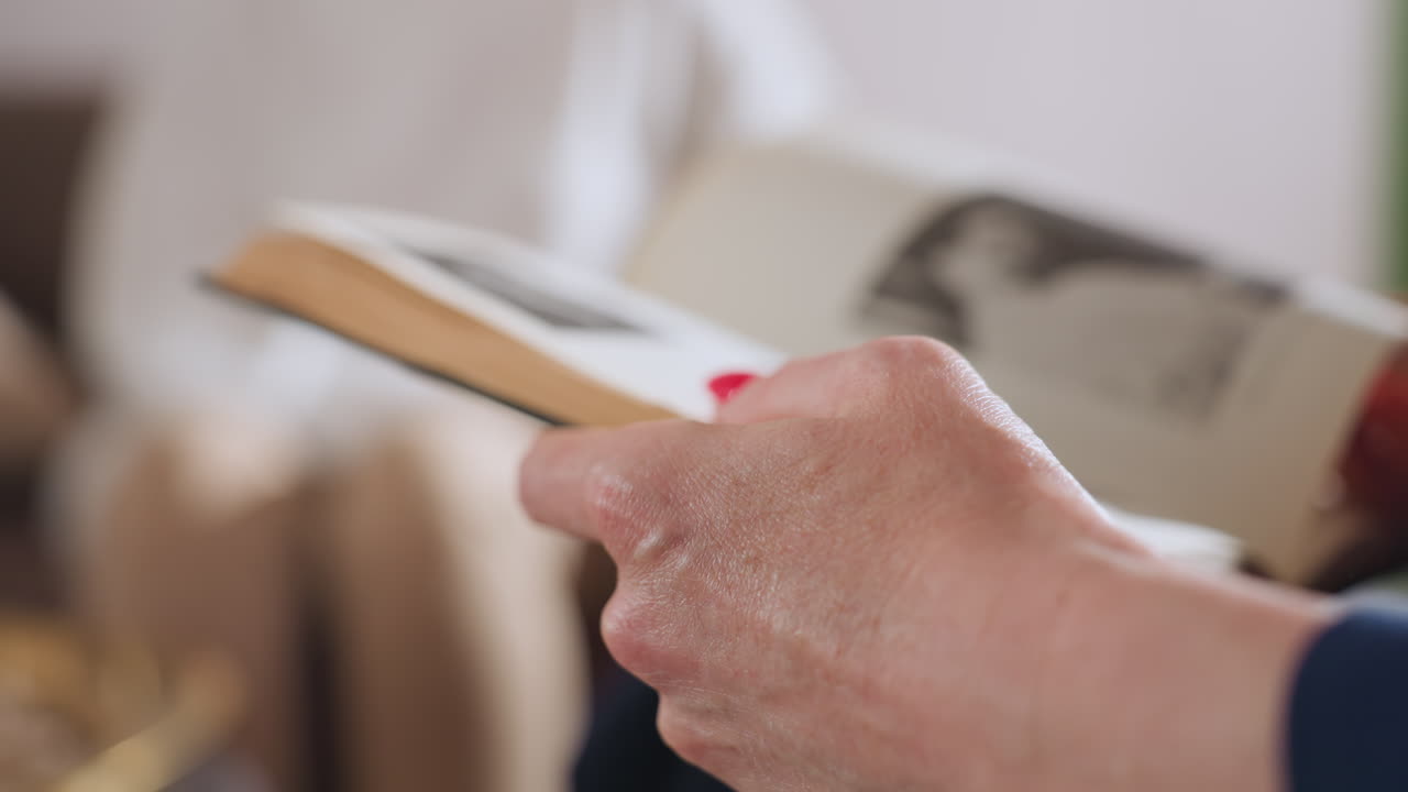 Close up of therapist hands with red manicure gently flipping through pages of open textbook in quiet setting, showing moment of focused attention and study during therapy or professional session
