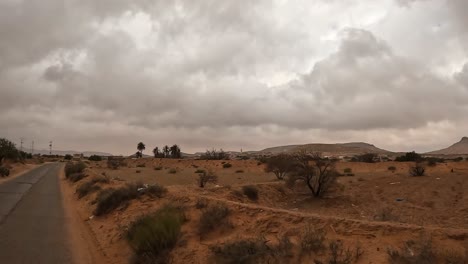 traveling by car through arid landscape of tunisia on cloudy stormy day, driver point of view