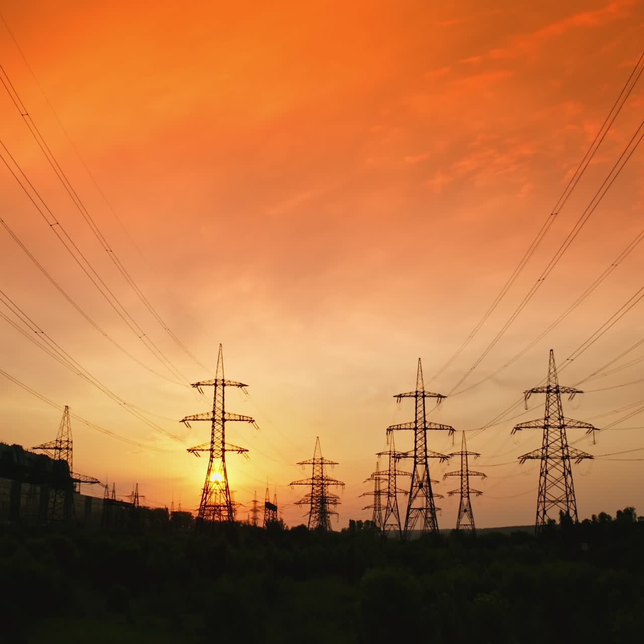 Transmission lines under red evening sky. High-voltage electric towers with wires in nature at beautiful sunset. Power lines against the backdrop of setting sun