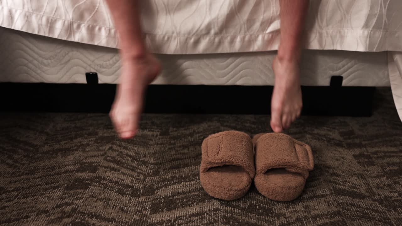 하 ⁇  남성 다리가 호텔 방 침대에서 나와 두꺼운 갈색 편안한 신발을 입고 멀리  ⁇ 고 있습니다.