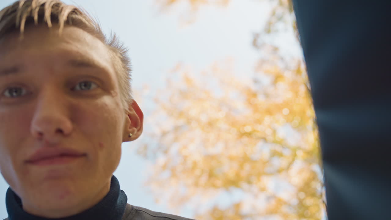 Ein weißer Mann schaut in eine Liefertasche, ein Kurier inspiziert ein Lebensmittelpaket unter einem Herbstbaum, niedriger Kamerawinkel, Hände greifen in die Tasche, neugieriger Ausdruck und überraschtes Lächeln, Sonnenlicht scheint durch gelbes Laub