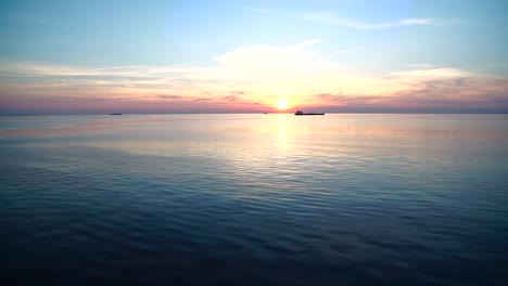 beautiful-sunset-over-the-horizon-of-the-ocean-sea-with-boats-cruising-in-front-of-the-low-sun,-dramatic-sunset-seen-from-cruise-ship