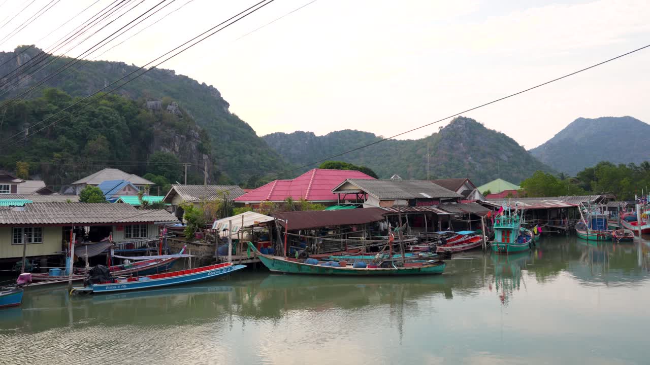 Colorful boats docked at a serene Thai village with mountains in the background, clear sky at dusk