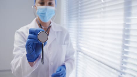 doctora caucásica con máscara facial y guantes quirúrgicos usando un estetoscopio