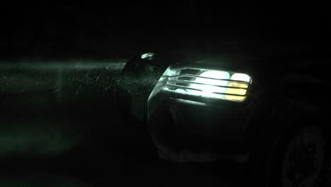 close up of a car headlight shining through a snowfall at night