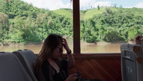 beautiful south east asian woman on a boat holding phone, mekong river lush green background