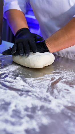 culinary specialist in black latex gloves kneading the dough. the cook prepares dough on a big metal table covered with flour. vertical video