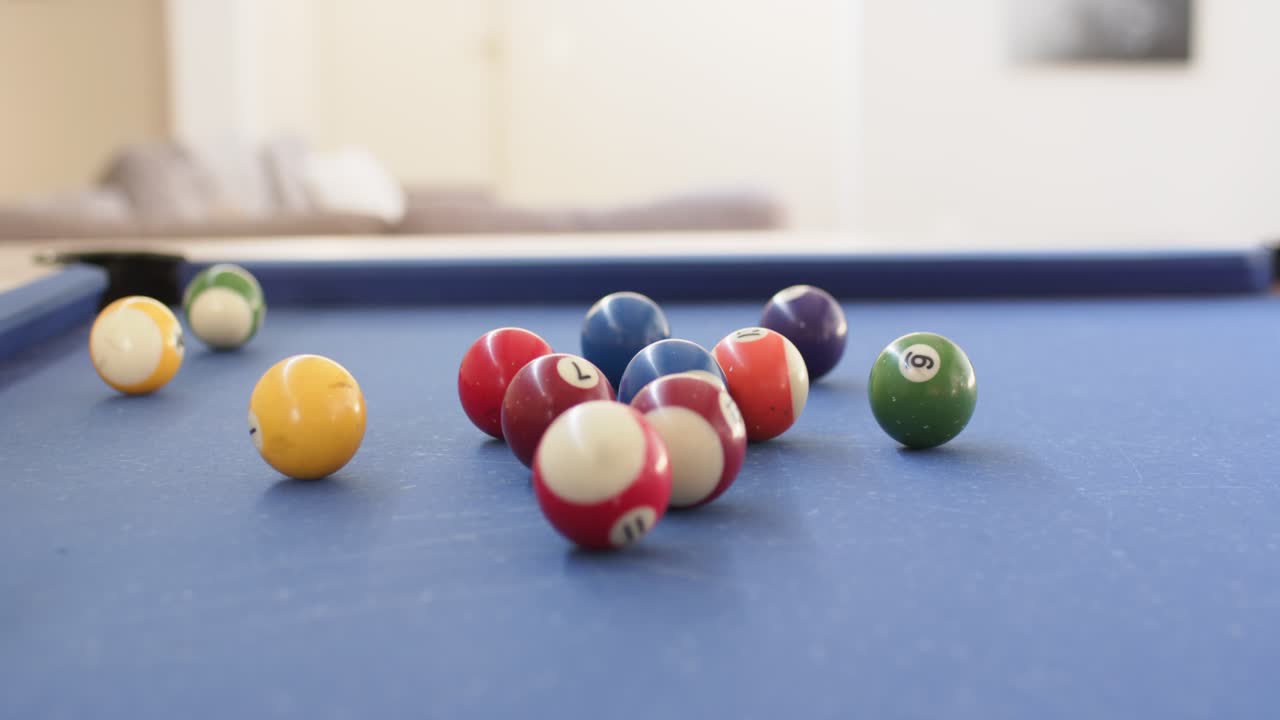 Unseen cue ball is striking clustered pool balls, scattering them on blue-felt table to start game