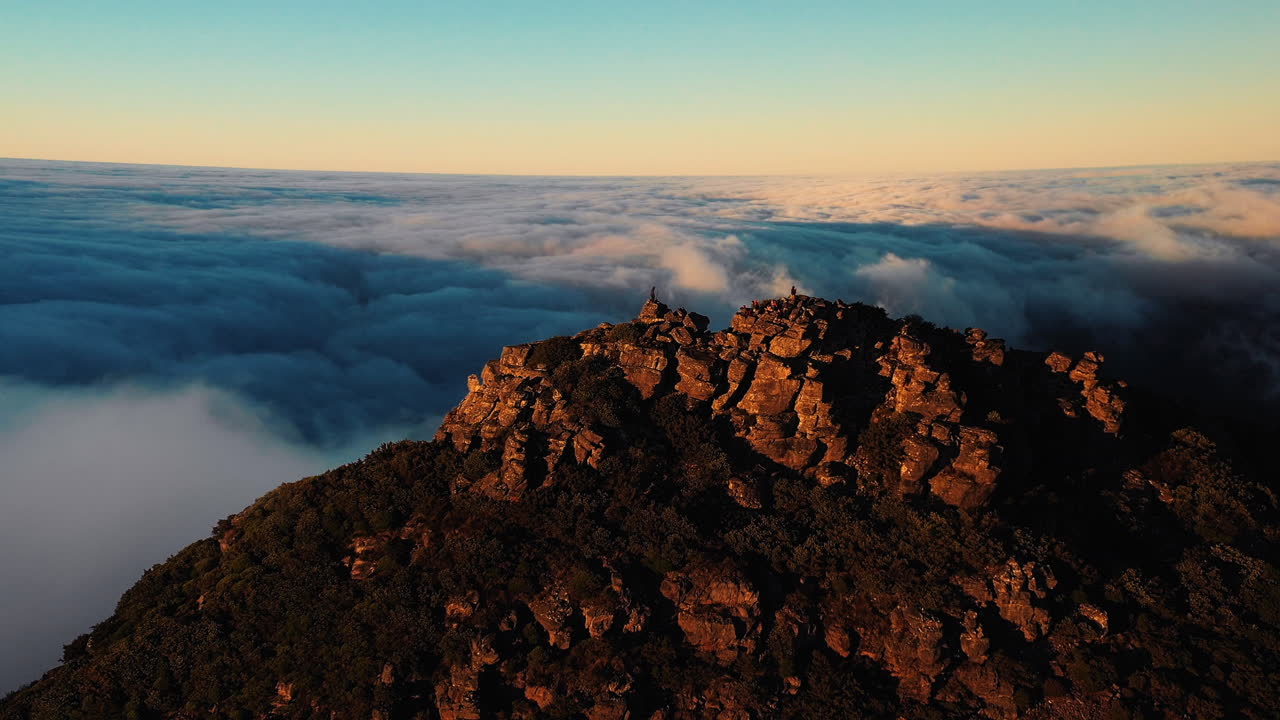 Aerial rising, drone shot tilting towards a person, standing on the top of the rocky mountain, above clouds, during sunset, in Hassell National Park, Great Southern region ,in West Australia