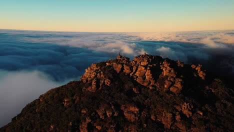 aerial rising, drone shot tilting towards a person, standing on the top of the rocky mountain, above clouds, during sunset, in hassell national park, great southern region ,in west australia