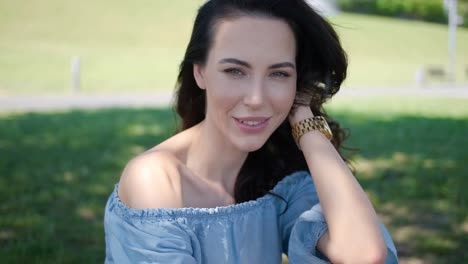 Portrait-of-attractive-brunette-woman-in-blue-dress-sitting-in-a-park