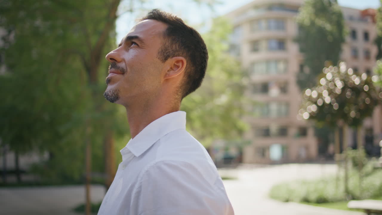 Smiling boss enjoying sunlight at summer city closeup. Brunette man at park