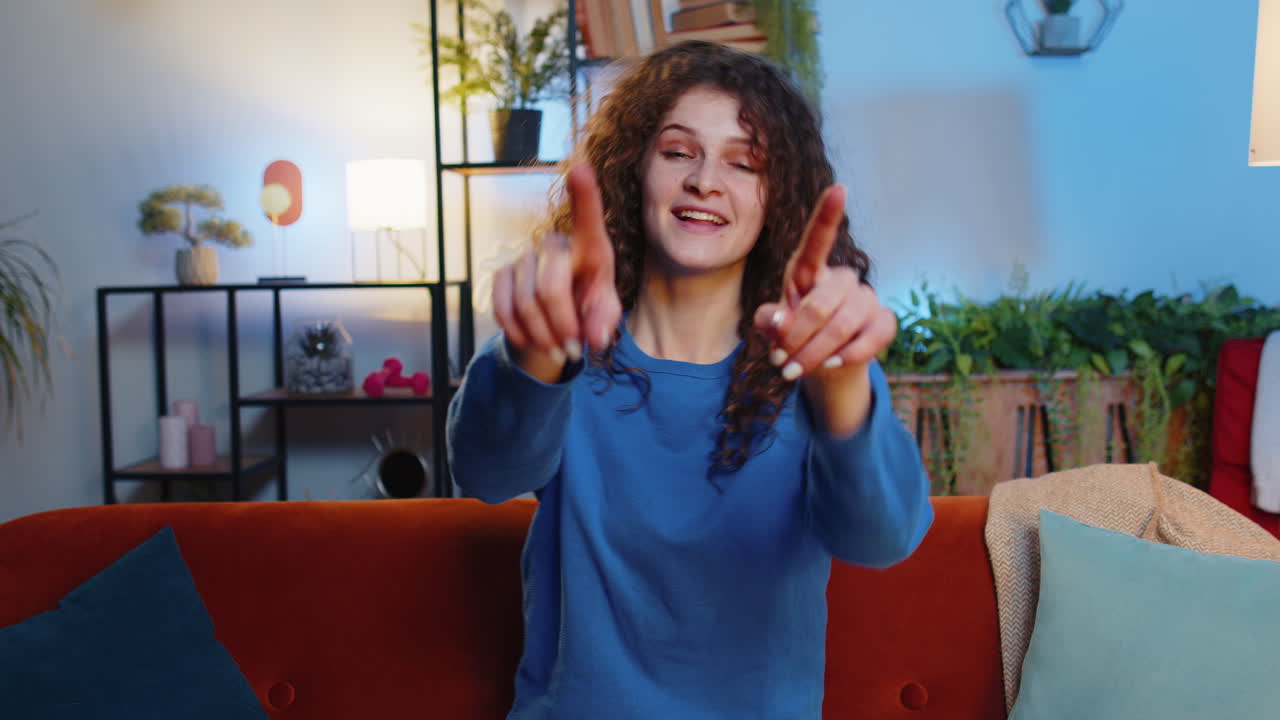 mujer feliz sentada en el sofá y señalando con ambas manos hace seleccionar y elegir el gesto